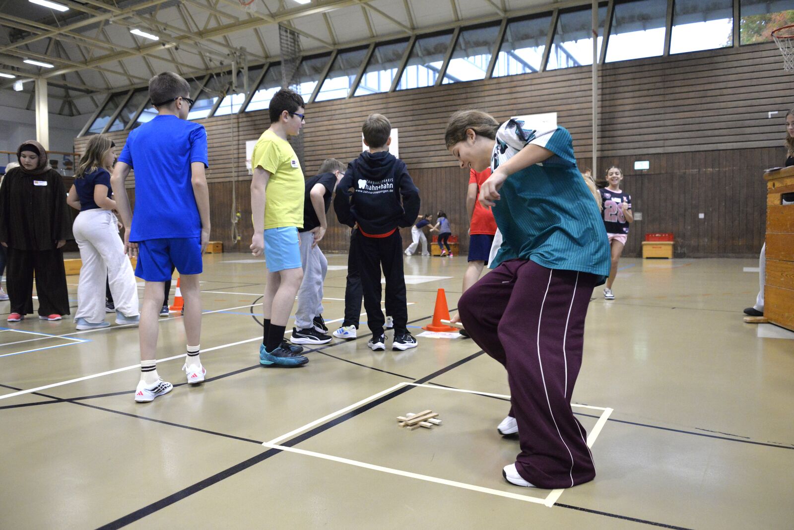 Schülerinnen und Schüler an einer Spielstation auf dem Hallenboden, ein Schüler beugt sich konzentriert nach vorn.