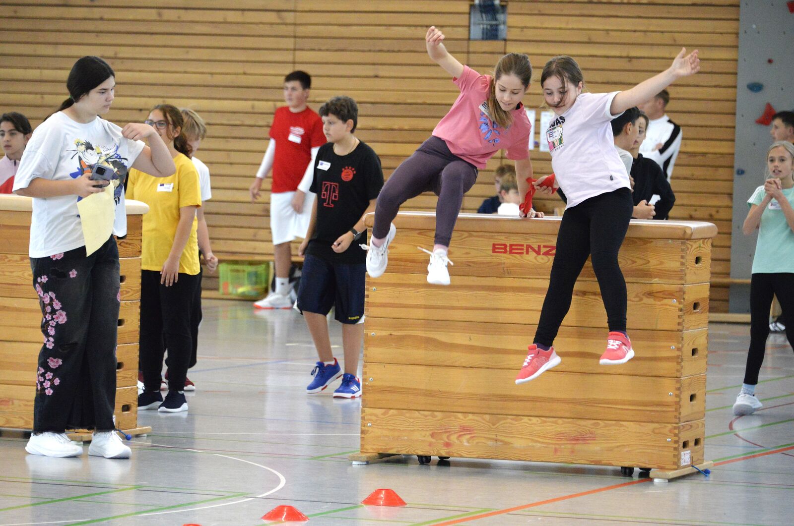 Zwei Mädchen springen im Parcours von einem Turnkasten, andere Kinder schauen zu.